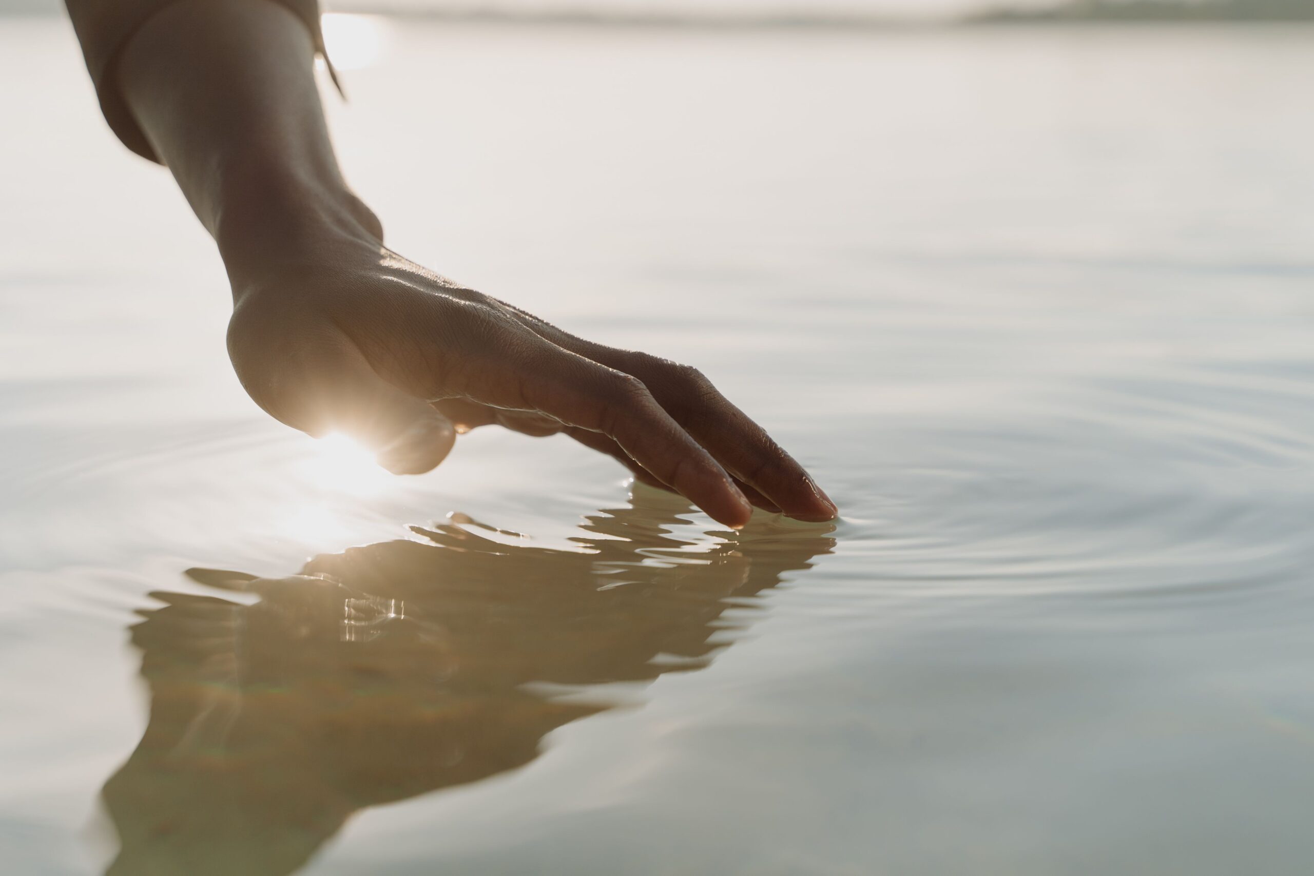 outdoor-image-02 A tranquil scene of a hand gently touching the water, creating ripples with gentle sunlight reflection.