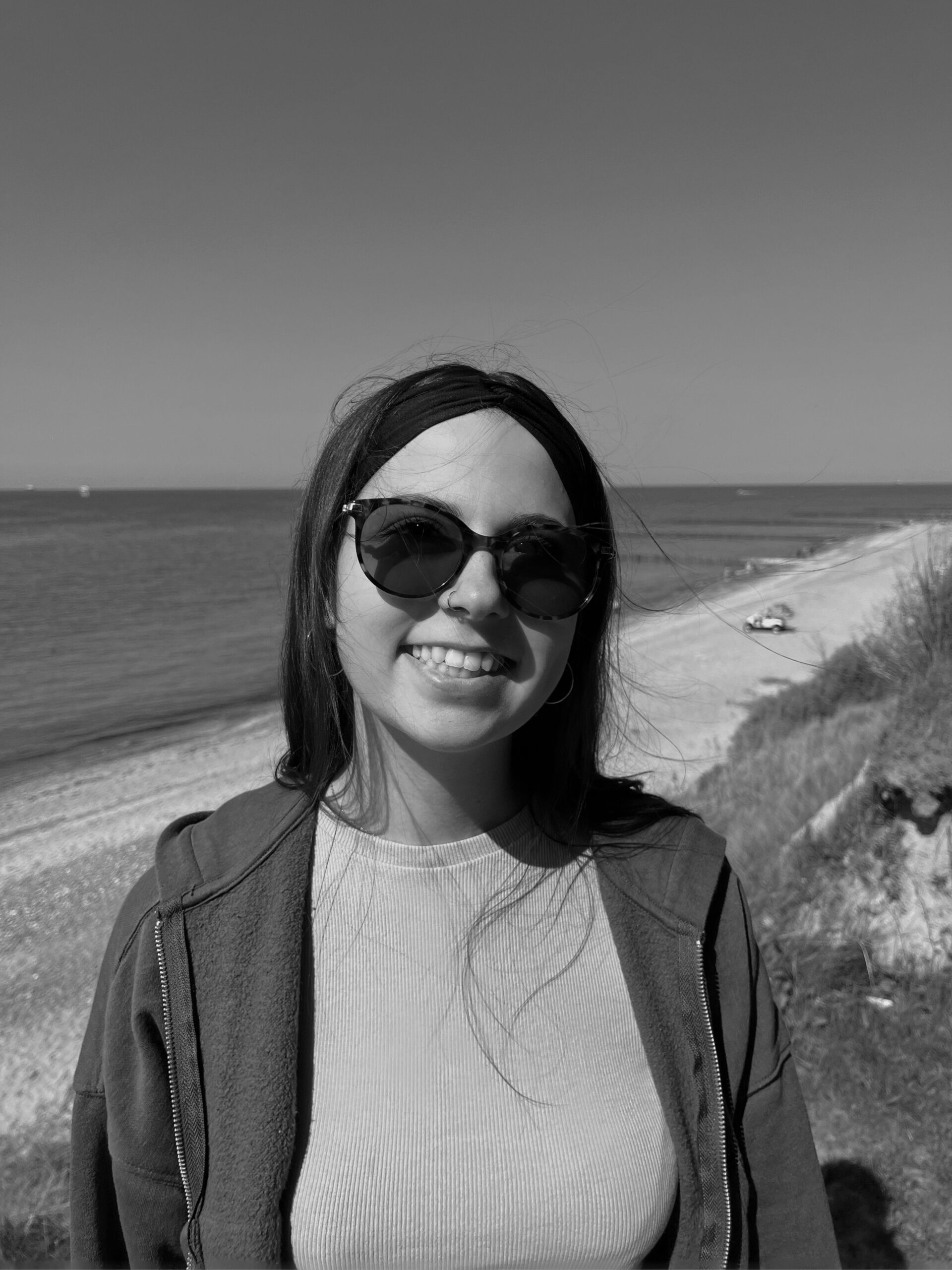 A young woman with sunglasses smiling on a beach in black and white.