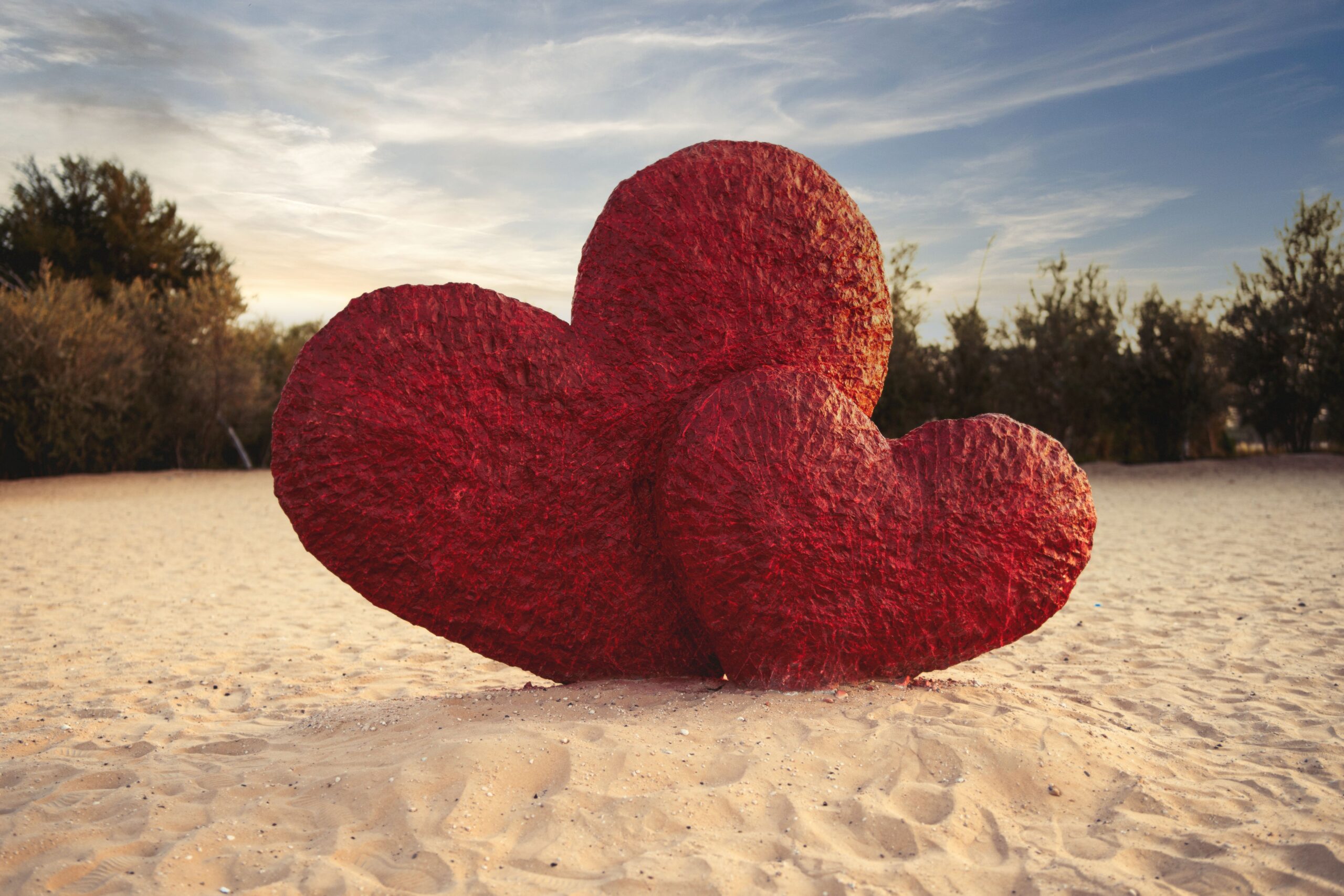 Large red heart sculptures on a sandy beach at daytime, symbolizing romance and love.