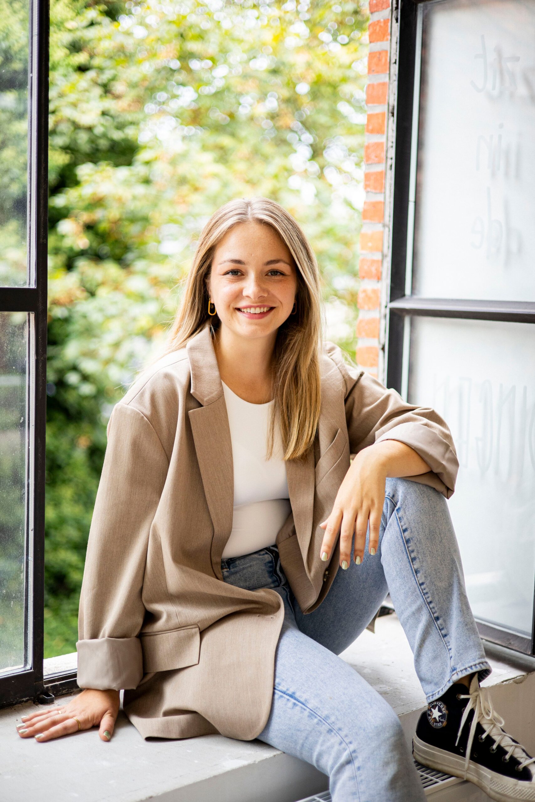 A relaxed and smiling woman sitting by an open window in natural light.