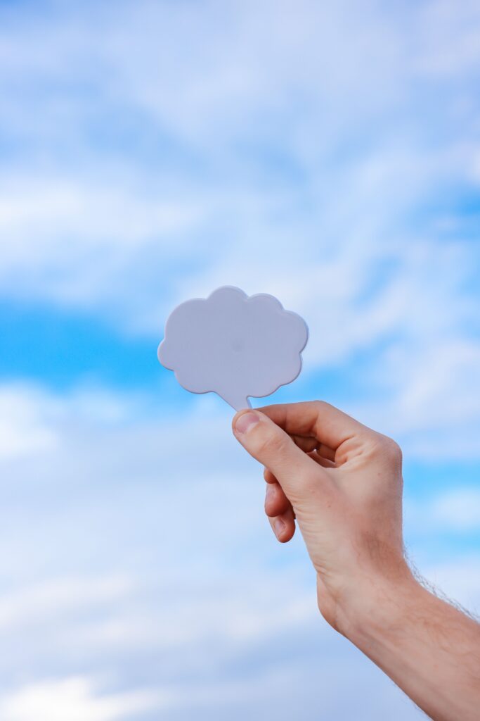 Close-up of a hand holding a cloud cutout with a bright blue sky background.